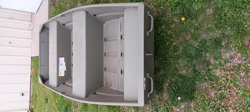 Slide: The Image of 2024 Tracker Grizzly 1236 Jon boat on grass, showcasing interior seating and storage. - 2