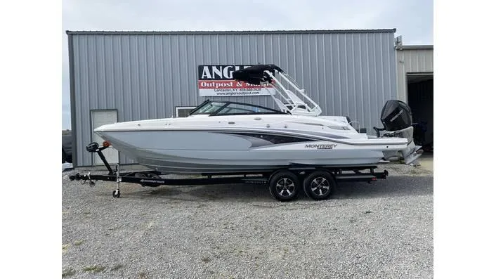 Slide: The Image of 2024 Monterey M-65 boat on trailer, parked outside a metal building. - 2
