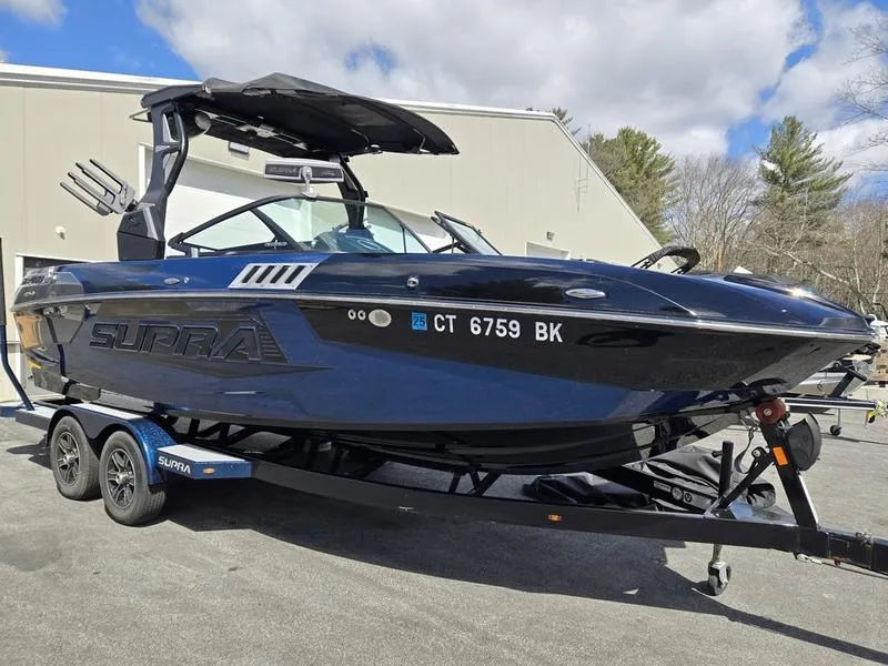Slide: The Image of 2019 Supra SA boat on trailer, black exterior, parked outdoors under cloudy sky. - 2
