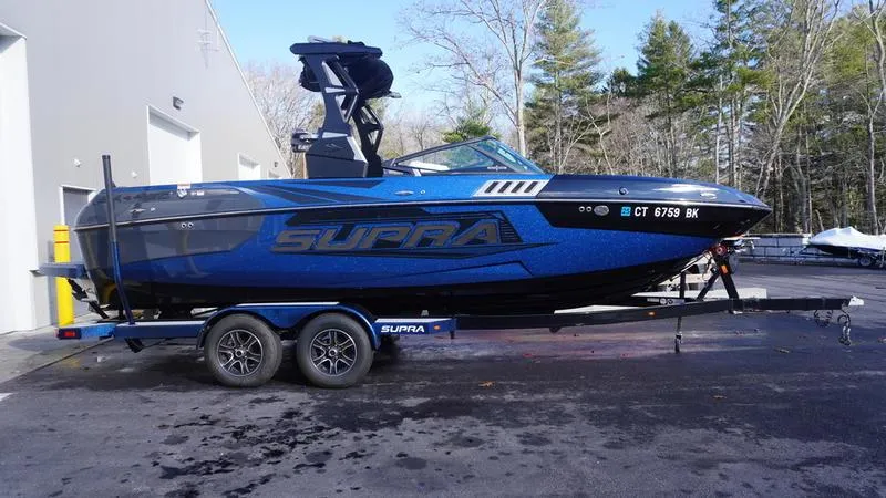 Slide: The Image of 2019 Supra SA boat on trailer, blue and black design, parked outdoors. - 20