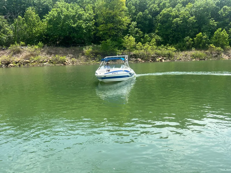 Slide: The Image of 2006 Larson Senza 206 boat cruising on a serene lake with lush green trees. - 10