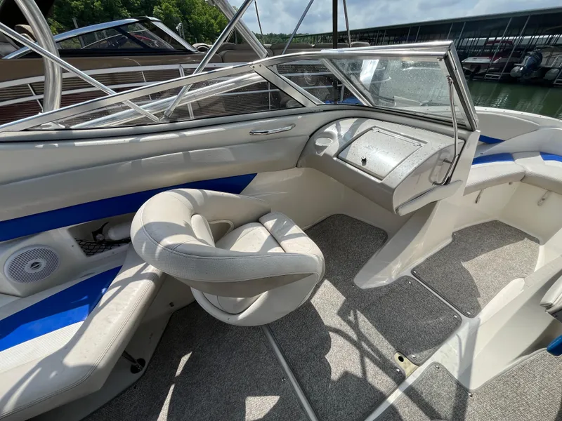 Slide: The Image of 2006 Larson Senza 206 boat interior with steering wheel and seating, docked by the water. - 13