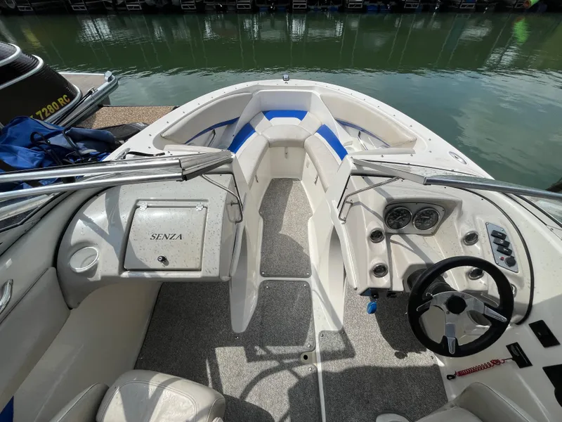 Slide: The Image of 2006 Larson Senza 206 boat interior with steering wheel and seating, docked by the water. - 15