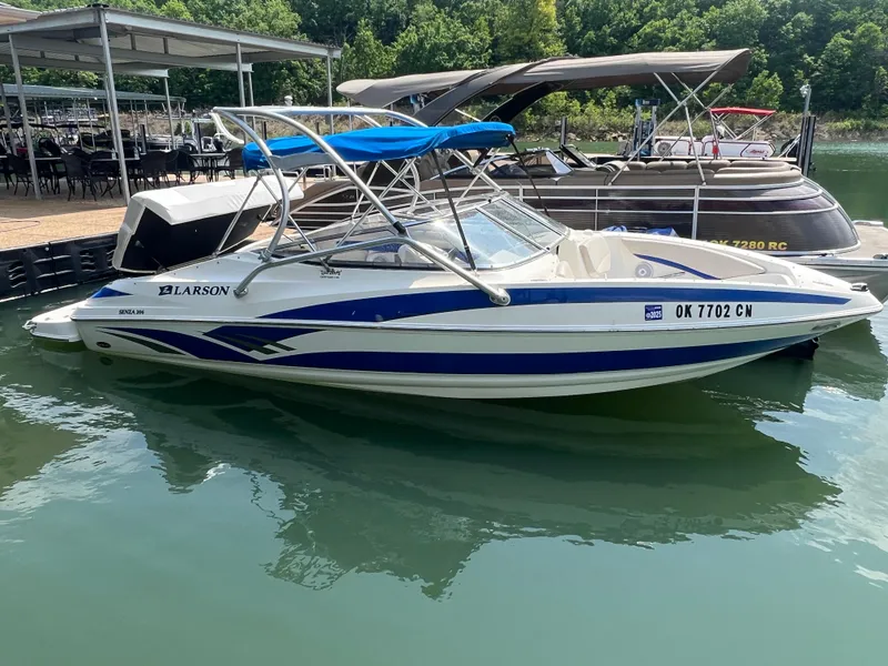 Slide: The Image of 2006 Larson Senza 206 boat docked on calm water with blue and white design. - 2