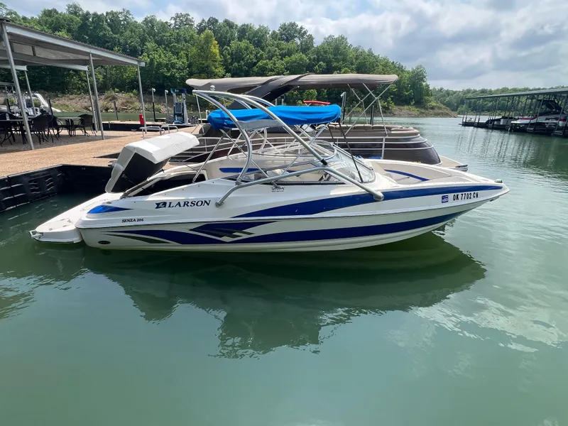 Slide: The Image of 2006 Larson Senza 206 boat docked on a calm lake with trees in the background. - 3