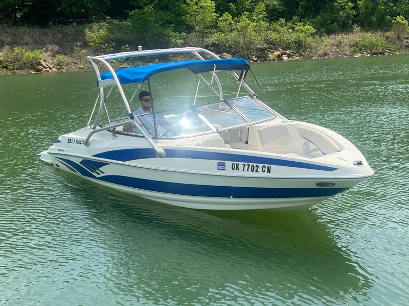 Slide: The Image of 2006 Larson Senza 206 boat with blue canopy cruising on a lake. - 6