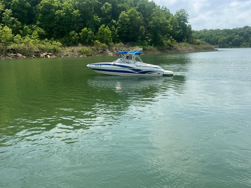 Slide: The Image of 2006 Larson Senza 206 boat on a calm lake with lush green shoreline. - 9