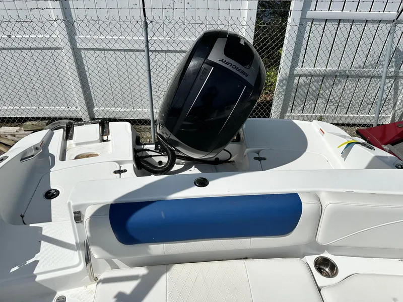 Slide: The Image of 2016 Tahoe 2150 Deck Boat with outboard motor, white and blue seating, fenced background. - 12