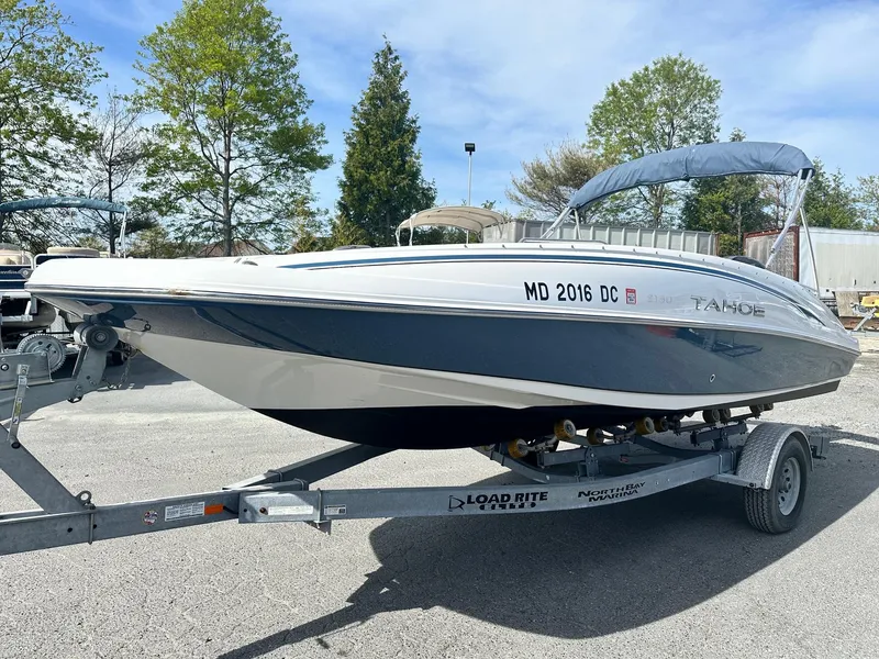 Slide: The Image of 2016 Tahoe 2150 Deck Boat on trailer, parked outdoors with trees in background. - 2