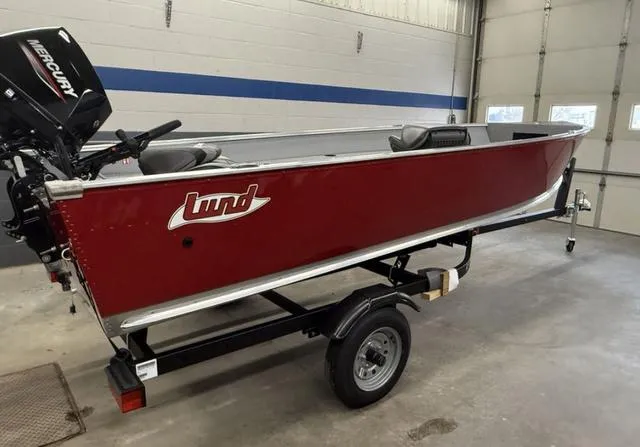 Slide: The Image of 2025 Lund 1600 Fury Tiller boat in a garage, red exterior, on a trailer. - 1