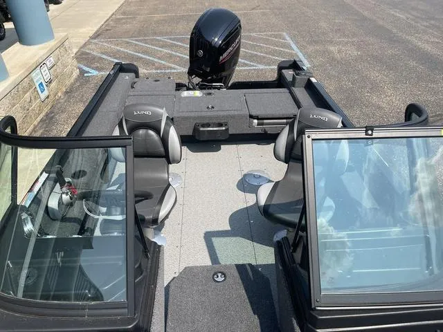 Slide: The Image of 2025 Lund 1775 Adventure Sport boat interior with seating and motor, parked on pavement. - 16