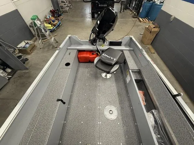 Slide: The Image of 2025 Lund 1600 Fury Tiller boat interior in a garage, featuring a motor and seating. - 13