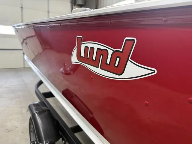 Slide: The Image of 2025 Lund 1600 Fury Tiller boat, red exterior, close-up of logo in a garage setting. - 5