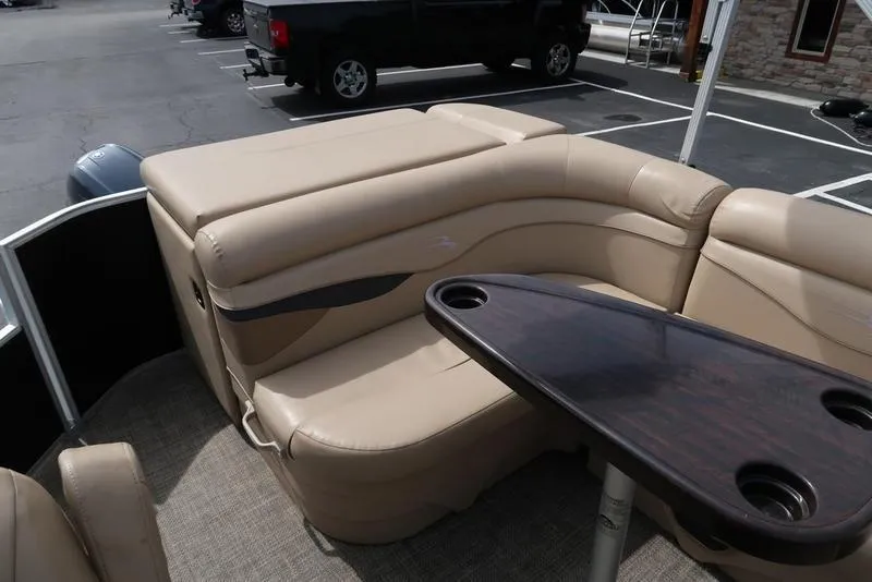 Slide: The Image of 2016 Bennington 22 SLX pontoon boat interior with beige seating and a dark wood table. - 17