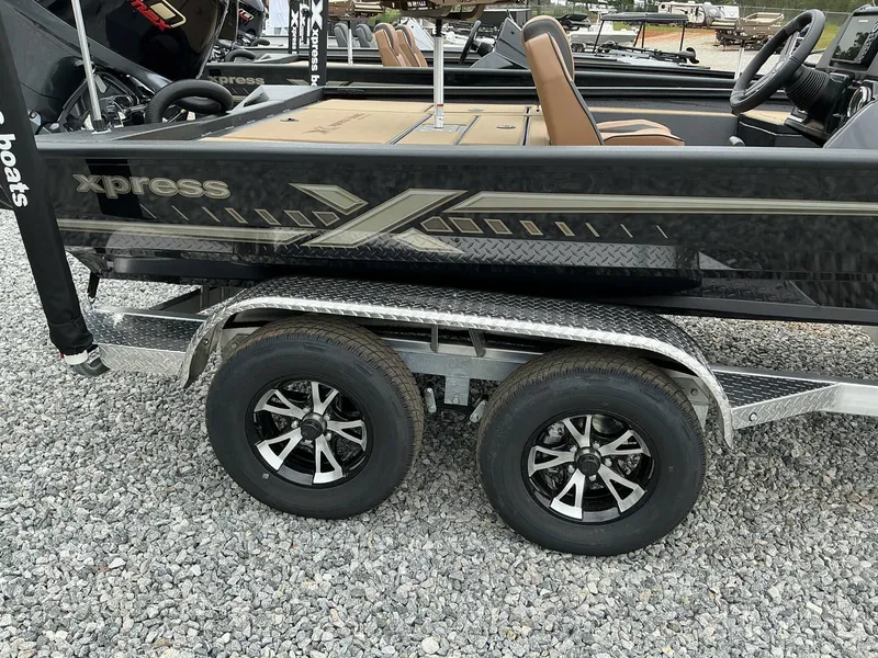 Slide: The Image of 2025 Xpress Hyper-Lift Crappie Series H20 boat on a dual-axle trailer, parked on gravel. - 10
