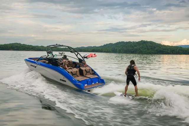 Slide: The Image of 2024 Yamaha Boats 222XD on lake, person wakesurfing behind, scenic landscape. - 7