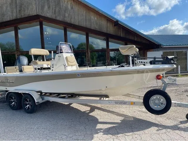 Slide: The Image of 2019 NauticStar 215 XTS boat on trailer, parked outside a rustic building. - 2