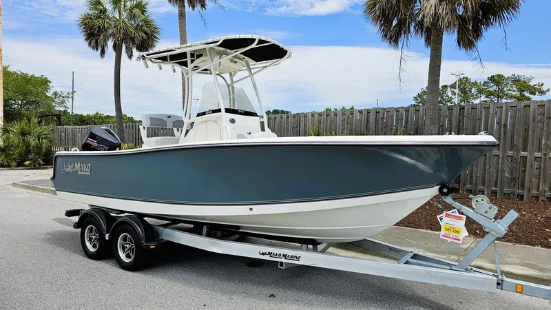 Slide: The Image of 2024 Mako 214 CC boat on trailer, parked near palm trees, under a clear sky. - 2