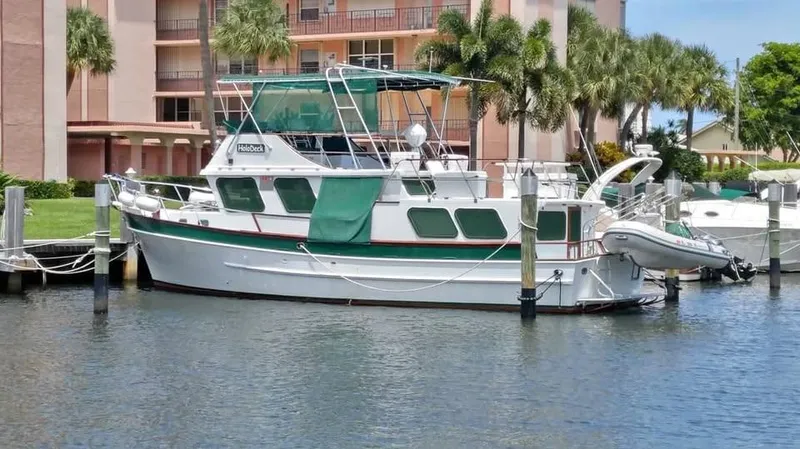 The Image of 1979 Universal Marine 41 boat docked in marina, surrounded by palm trees and buildings. - 0