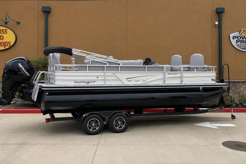 Slide: The Image of 2025 Ranger Reata 223FC pontoon boat on trailer, parked outside a store. - 77