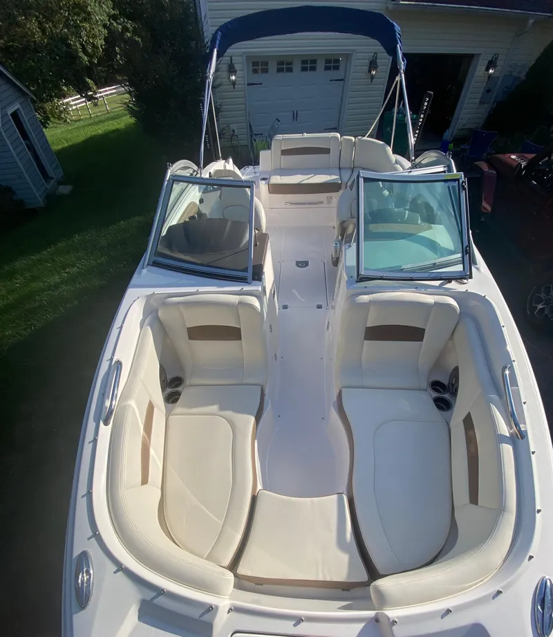 Slide: The Image of 2014 Chaparral 224 Sunesta boat with open seating and canopy, parked near a garage. - 33