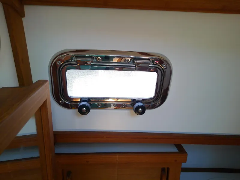 Slide: The Image of Porthole window inside 2017 Com-Pac 27/3 sailboat, featuring wooden interior accents. - 47