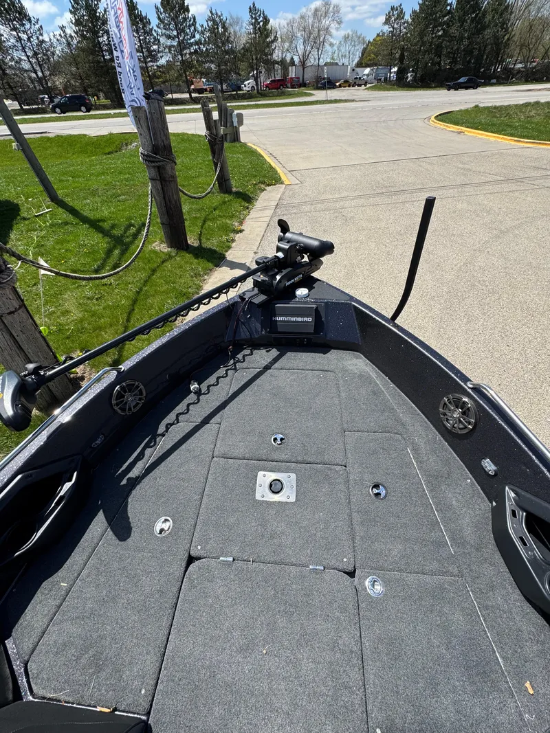 Slide: The Image of 2022 Skeeter Solera 205 boat deck with fishing equipment, parked near trees and grass. - 18