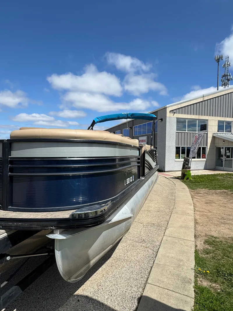 Slide: The Image of 2018 Harris Grand Mariner 230 pontoon boat parked near a modern building under a blue sky. - 8