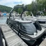Slide: The Image of 2022 Bennington QX 23 Quad Bench pontoon boat docked by a scenic lakeside. - 3