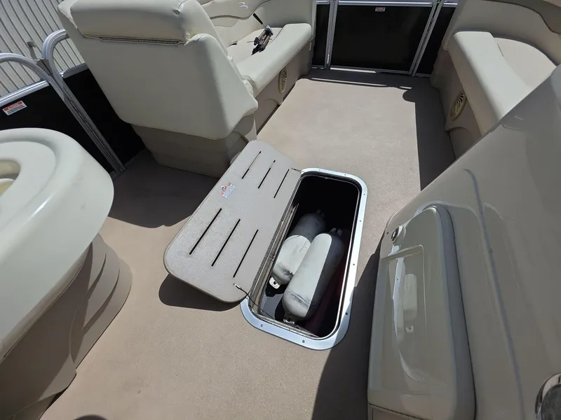 Slide: The Image of 2013 Bennington 24 SSLX boat interior with open storage compartment and beige seating. - 15