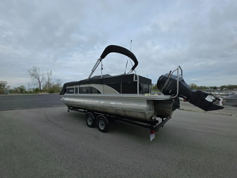 Slide: The Image of 2013 Bennington 24 SSLX pontoon boat on trailer, parked outdoors under cloudy sky. - 2