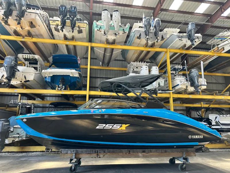 The Image of 2023 Yamaha Boats 255XD in storage, vibrant blue and black design, surrounded by other boats. - 0