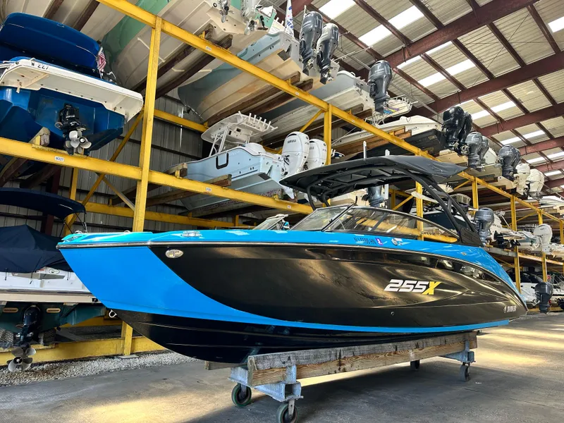 Slide: The Image of 2023 Yamaha Boats 255XD in storage, vibrant blue and black design, indoor warehouse setting. - 1