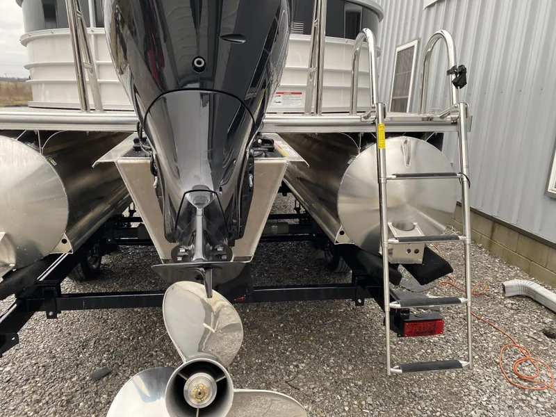 Slide: The Image of 2024 Berkshire 24RFX LE pontoon boat with outboard motor and ladder, parked on gravel. - 11