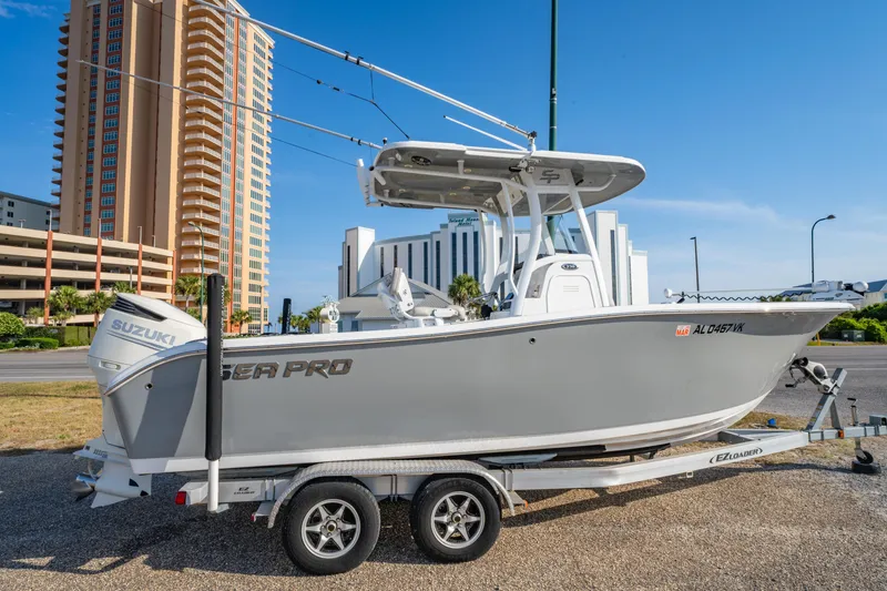 Slide: The Image of 2019 Sea Pro 239 DLX boat on trailer, parked near tall buildings under clear blue sky. - 2