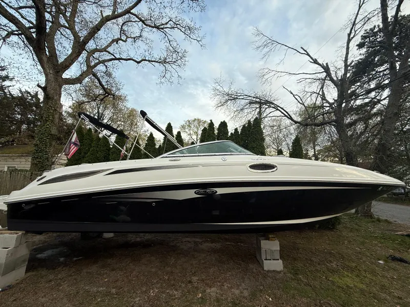 The Image of 2012 Sea Ray 280 Sundeck boat on land, surrounded by trees and flags. - 1