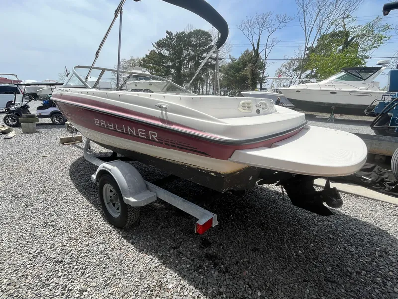 Slide: The Image of 2011 Bayliner 195 boat on trailer, parked on gravel lot, surrounded by other boats. - 6