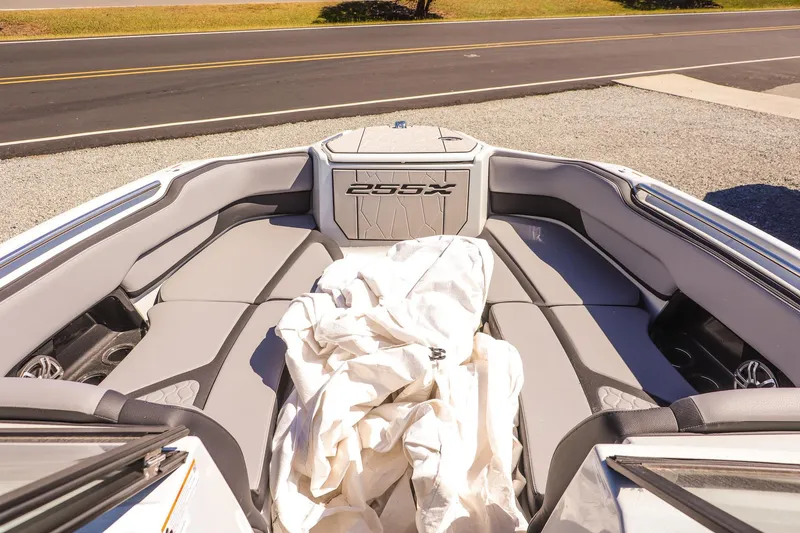 Slide: The Image of 2025 Yamaha Boats 255XD interior with gray seating and cover, parked on gravel near road. - 15