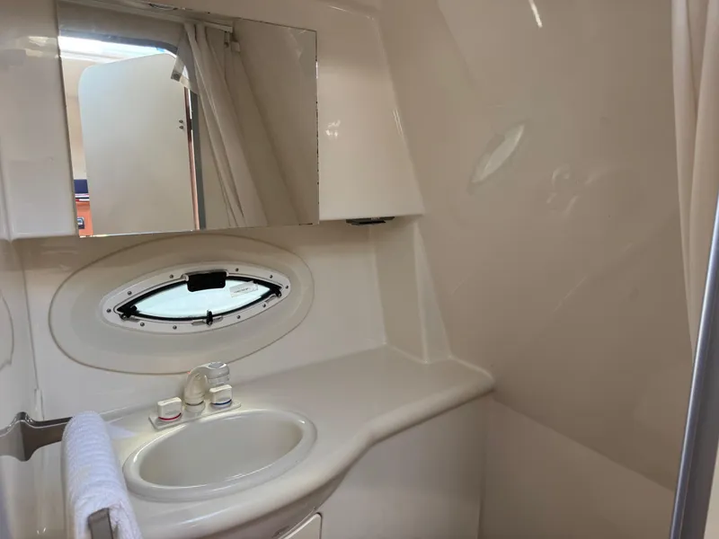 Slide: The Image of 2008 Bayliner 265SB boat bathroom with sink, mirror, and porthole window. - 16