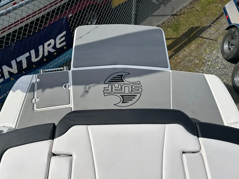 Slide: The Image of 2019 Chaparral 23 H2O Surf boat deck with "Surf" logo, parked near a fence. - 10