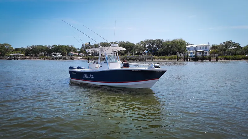 Slide: The Image of 2006 Regulator 26 FS boat on calm water, clear sky, and shoreline in the background. - 2