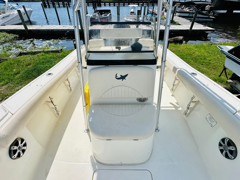 Slide: The Image of 2014 Mako 204 CC boat interior with seating and steering console, docked by the water. - 12