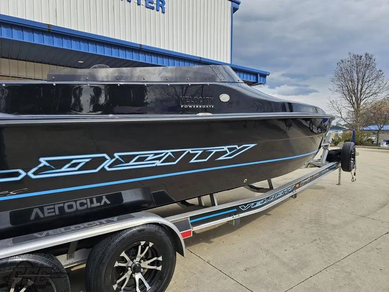 Slide: The Image of 2022 Velocity 290SC Signature Series boat on trailer, black with blue accents, parked outdoors. - 11