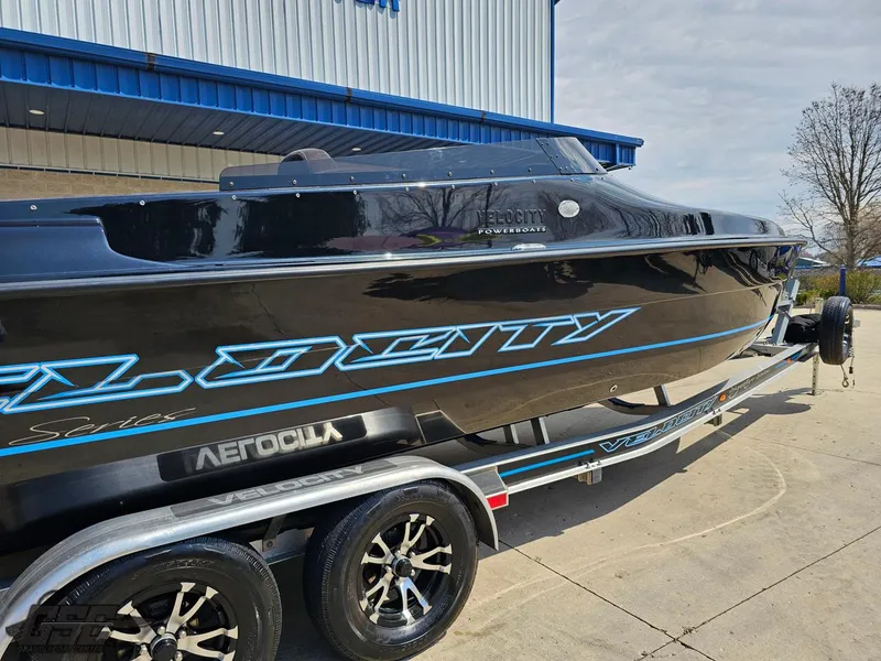 Slide: The Image of 2022 Velocity 290SC Signature Series boat on trailer, black with blue accents, parked outdoors. - 7