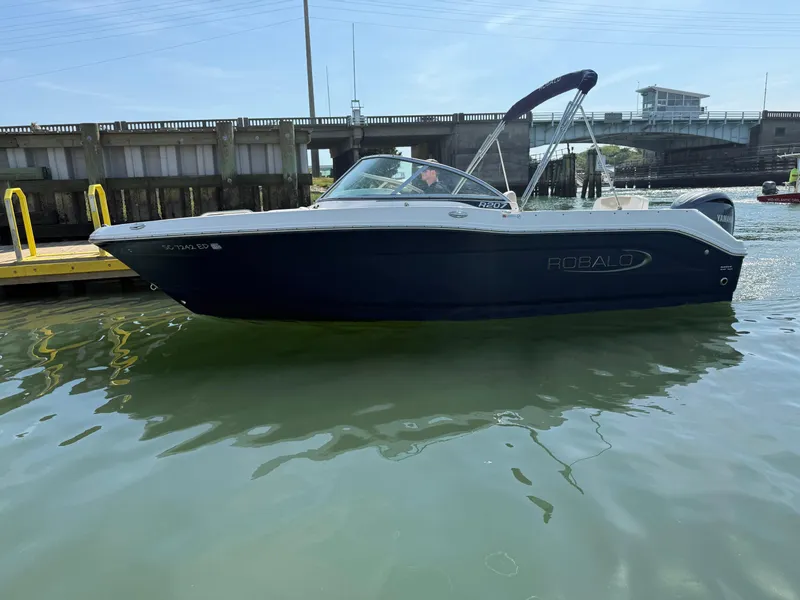 Slide: The Image of 2024 Robalo R207 Dual Console boat on water near a dock and bridge. - 34