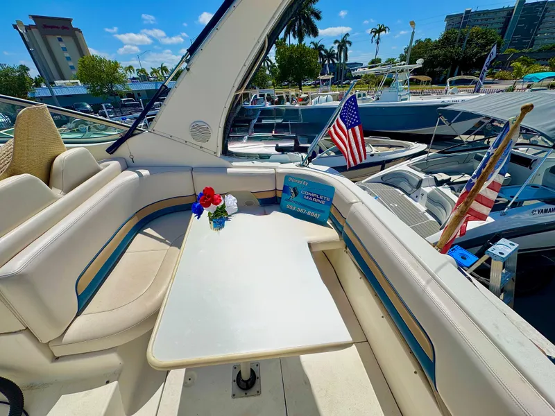 Slide: The Image of 1999 Chaparral 290 Signature Cruiser interior with table, seating, and American flag at marina. - 4