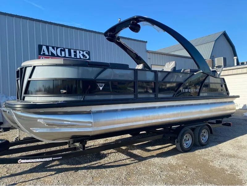 Slide: The Image of 2024 Trifecta 23 RFS 3.0 pontoon boat on trailer, parked outside Anglers building. - 24