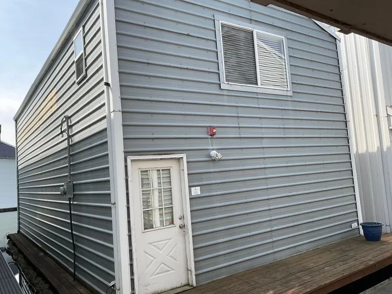 The Image of Custom 1987 boathouse with gray siding, white door, and wooden deck. - 1