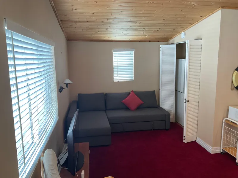 Slide: The Image of Cozy boathouse interior with red carpet, gray sofa, and wooden ceiling, featuring natural light. - 5