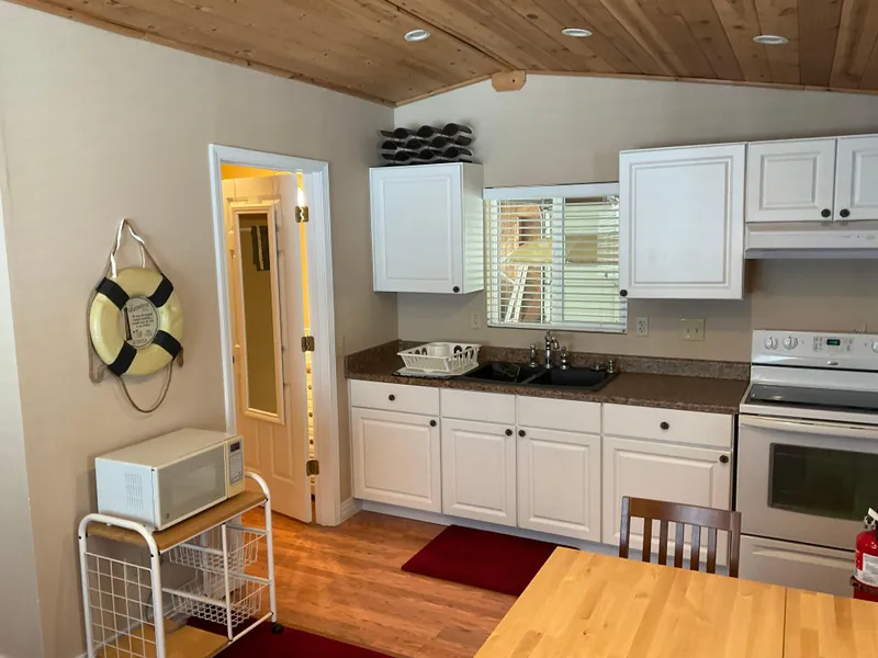 Slide: The Image of Cozy boathouse kitchen with white cabinets, wooden ceiling, and modern appliances, built in 1987. - 7